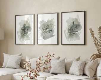 May include: Three framed watercolor paintings with Arabic calligraphy in green and white on a beige background. The paintings are hanging on a wall above a white sectional sofa with pillows.