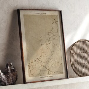 May include: Framed vintage-style map print of Cagayan, Philippines. The map features a network of lines and text at the top and bottom. The print is in a dark wooden frame and is displayed on a white shelf. Coordinates are visible at the top.
