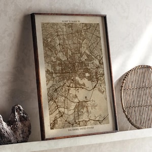 May include: A framed sepia-toned map of Baltimore, Maryland, showing the city's street layout and waterways. The map is labelled "Baltimore, United States" and includes coordinates. The frame is dark brown.