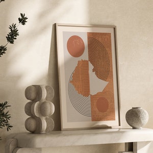 Może przedstawiać: Wydruk abstrakcyjny w ramie z geometrycznymi kształtami w odcieniach brązu i beżu. Wydruk wisi na białej ścianie nad marmurowym stolikiem konsolowym z dwoma ozdobnymi wazami.