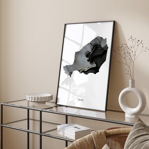 May include: A black and white abstract art print of the country of Niger. The print is framed in a black frame and is hanging on a wall above a glass-top table.