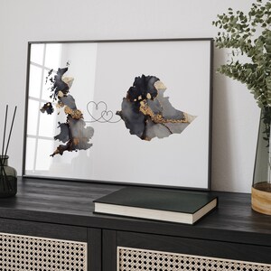 Może przedstawiać: Wydruk w ramie z czarno-białą mapą Wielkiej Brytanii i Etiopii połączonych linią z dwoma sercami. Mapa znajduje się na białym tle z złotymi akcentami.