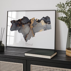 May include: A framed print of a black and gold abstract design representing the city of Peterborough, Cambridgeshire. The print is on a white background and has a black frame.