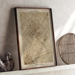 May include: A framed vintage map print of Guelph, Canada, in a brown wooden frame. The map shows detailed street layouts and geographical features. The text "Guelph, Canada" is at the bottom. Coordinates are displayed at the top.