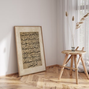 May include: A framed print of a black and white Arabic calligraphy design on a beige background. The calligraphy is in a traditional style and is framed in a simple wooden frame.