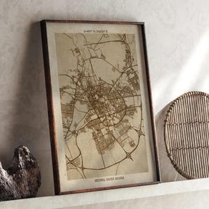 Può includere: Stampa incorniciata della mappa di Medina, Arabia Saudita, in tonalità seppia. La mappa dettagliata della città è racchiusa in una cornice di legno marrone scuro. Le coordinate sono stampate in alto. La stampa è esposta su una mensola bianca.