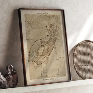 May include: Framed map print of St. John's, Canada, in sepia tones. The map shows roads and city layout, with coordinates at the top. The print is in a dark brown wooden frame, with the text "ST. JOHN'S, CANADA" at the bottom.