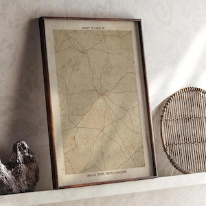 Może przedstawiać: Oprawiony wydruk mapy w stylu vintage z Omagh Town, Wielka Brytania. Mapa przedstawia sieć dróg w brązowym tuszu na beżowym tle. Wydruk jest w ciemnobrązowej drewnianej ramie.