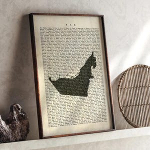 May include: Framed print featuring a map of the UAE in a dark silhouette against a vintage-style background filled with text. The print is encased in a dark brown wooden frame, suitable for home decor.