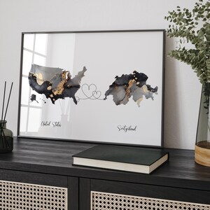 May include: A framed print with a black and white watercolor map of the United States and Switzerland connected by a line with two hearts. The text "United States" and "Switzerland" is below each map.