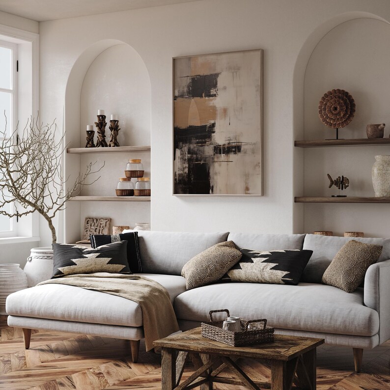 May include: A white sectional sofa with a light brown throw blanket,  three pillows with black and white geometric patterns, and a wooden coffee table with a woven basket on top. The sofa is in a living room with white walls and arched doorways.