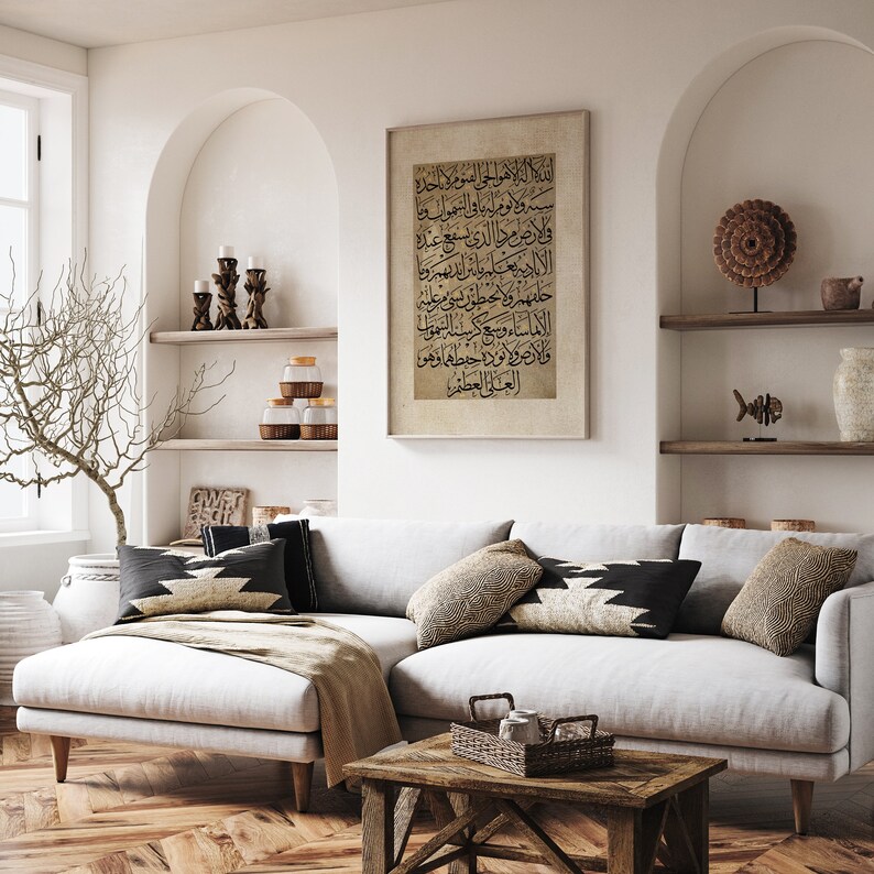 May include: A white sectional sofa with black and white patterned throw pillows in a living room setting. A framed print with Arabic calligraphy hangs on the wall above the sofa. The sofa is in front of a wooden coffee table with a woven basket on top.