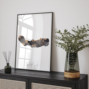 Peut inclure: Une impression abstraite en noir et or de l'île de São Miguel, Açores. L'impression est encadrée dans un cadre noir et est accrochée à un mur blanc.