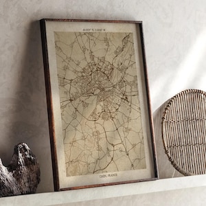 Puede incluir: Mapa en tonos sepia enmarcado de Caen, Francia, con coordenadas en la parte superior. El mapa presenta detalles de carreteras y edificios, en un marco de madera marrón oscuro. El texto "CAEN, FRANCE" está en la parte inferior.