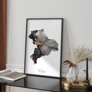 May include: A black framed print with a gray and gold abstract design of the Hackney borough in London. The text "Hackney London" is printed below the design.