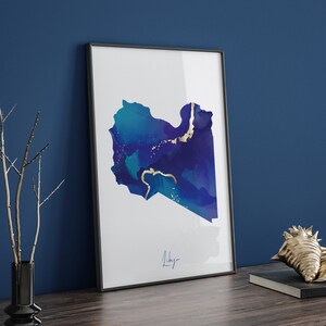 Puede incluir: Una impresión enmarcada de un mapa abstracto de Libia en tonos azules y dorados. La palabra "Libia" está escrita en letras doradas en la parte inferior de la impresión.