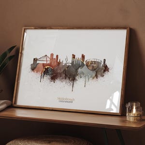 Könnte beinhalten: Gerahmter Kunstdruck mit einer Skyline von Middlesbrough, Vereinigtes Königreich, im Aquarellstil. Das Kunstwerk verwendet Braun-, Grau- und Goldtöne vor einem weißen Hintergrund. Der Text "Middlesbrough UNITED KINGDOM" ist unten zu sehen.