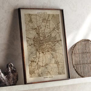 May include: Framed map of Rennes, France, in sepia tones. The map details the city's roads and infrastructure, with the text "RENNES, FRANCE" at the bottom. Coordinates are printed at the top. The frame is dark brown.