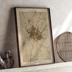 May include: Framed vintage-style map of Colima, Mexico, in sepia tones. The map features intricate street details and is encased in a dark wooden frame. Coordinates are printed at the top. The city name is printed at the bottom.