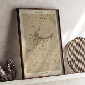 May include: Framed map print of Obuasi, Ghana, showing a network of roads and streets in brown against a beige background. The frame is dark brown. The text "6.3002° N, 1.0015° W" and "Obuasi, Ghana" are visible.
