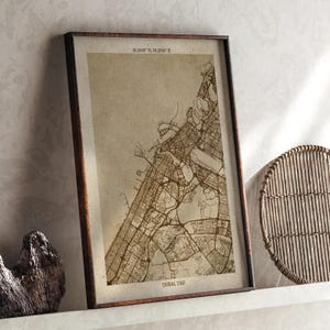 May include: A framed map of Dubai, UAE, in sepia tones. The map details the city's layout, with streets and landmarks visible. The frame is dark brown. Coordinates 25.2048° N, 55.2700° E are printed at the top. The text "DUBAI UAE" is at the bottom.