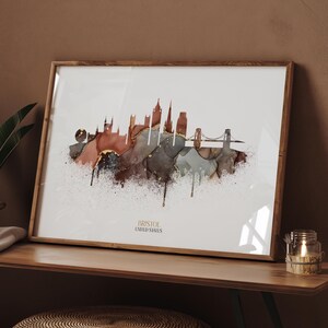 May include: A framed art print showcasing a watercolour-style representation of the Bristol, United States skyline. The artwork uses brown, grey, and gold tones against a white backdrop. The text "BRISTOL UNITED STATES" is printed at the bottom.