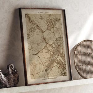 May include: A framed map print of Penarth, United Kingdom, in sepia tones. The map details the town's layout with roads and buildings. The frame is dark brown, and the text "PENARTH UNITED KINGDOM" is at the bottom.