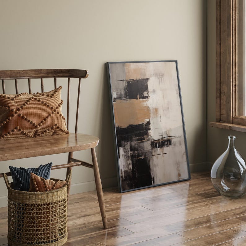 May include: A wooden bench with a brown cushion and two smaller cushions in blue and brown. A framed abstract painting with black, white, and brown brushstrokes hangs on the wall behind the bench.