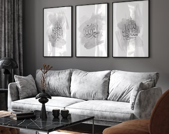 May include: Three framed prints with a gray watercolor background and black Arabic calligraphy. The prints are hanging on a gray wall above a gray couch.
