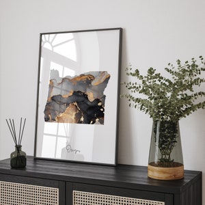 Könnte beinhalten: Gerahmter Kunstdruck mit einem abstrakten Design in Form des Bundesstaates Oregon. Das Kunstwerk zeigt eine Mischung aus Schwarz-, Grau- und Goldtönen, die eine moderne und elegante Ästhetik erzeugt. Das Wort "Oregon" ist darunter in Schreibschrift geschrieben.