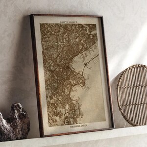Puede incluir: Impresión enmarcada de un mapa de Yokohama, Japón, en tonos sepia. El mapa detalla el diseño de la ciudad, incluyendo calles y vías fluviales. La impresión está en un marco marrón oscuro e incluye el texto "YOKOHAMA, JAPAN" en la parte inferior.