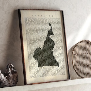 Pode incluir: Impressão emoldurada com um mapa dos Camarões em silhueta escura sobre um fundo de estilo vintage. A palavra "CAMEROON" está impressa no topo. A impressão está em uma moldura marrom escura e é exibida em uma prateleira branca.