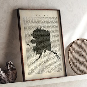 May include: A framed print showing a map of Alaska in a dark silhouette against a vintage-style background filled with text. The frame is a dark brown colour. The word "ALASKA" is at the top of the print.