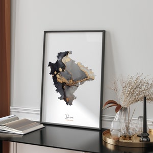 May include: A black and white abstract art print of the Devon region of England with gold accents. The print is framed in a black frame and is hanging on a white wall.