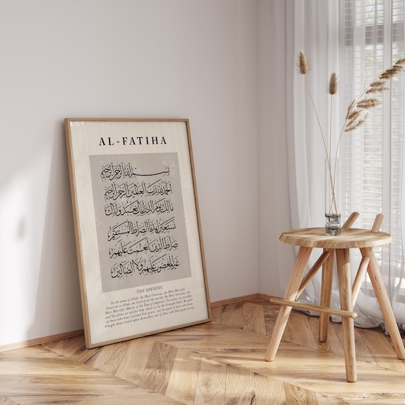 May include: A framed print with the title "AL-FATIHA" in black text. The print features Arabic calligraphy in black on a beige background. The text below the calligraphy reads "THE OPENING" and includes a translation of the Arabic text.