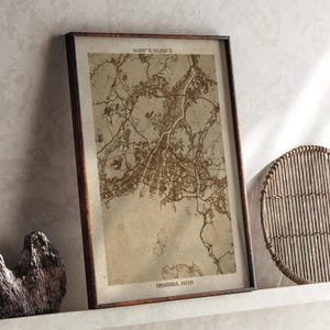 Puede incluir: Impresión enmarcada de un mapa de Hiroshima, Japón, en tonos sepia. El mapa detallado de la ciudad muestra carreteras, vías fluviales y edificios. El marco es de color marrón oscuro. Las coordenadas están impresas en la parte superior.