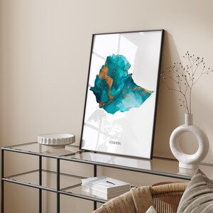 Może przedstawiać: Wydruk w ramie przedstawiający abstrakcyjną mapę Etiopii w kolorze turkusowym i złotym. Mapa jest obwiedziona czarną linią, a słowo "Etiopia" jest nadrukowane na dole wydruku czarnym kolorem.