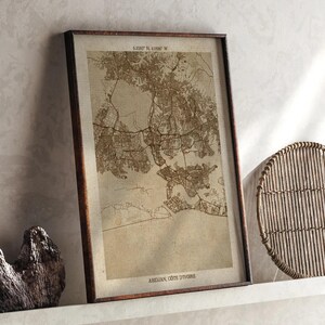 May include: Framed map print of Abidjan, Côte d'Ivoire, in sepia tones. The map shows the city's layout, with streets and waterways. The frame is dark brown, and the print is displayed on a white shelf.