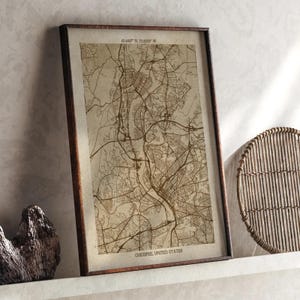 Puede incluir: Impresión enmarcada del mapa de Chicopee, Estados Unidos, en tonos sepia. El mapa muestra el diseño de la ciudad con carreteras y edificios. El marco es de color marrón oscuro. Las coordenadas son visibles en la parte superior del mapa.