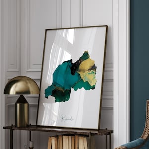 May include: A minimalist art print featuring a teal and gold abstract design of the country of Rwanda. The print is framed in a thin gold frame and has the word "Rwanda" written in cursive at the bottom.
