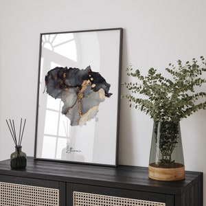 May include: A black and gold abstract art print of the country of Lithuania. The print is framed in a black frame and is hanging on a white wall.