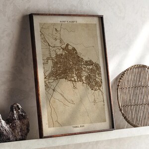May include: A framed map print of Tabriz, Iran, in sepia tones. The map details the city's layout with streets and buildings. The frame is a dark brown, and the print includes the city's name and coordinates.