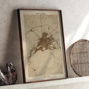 May include: Framed map print of Arak, Iran, in sepia tones. The map details the city's layout with roads and buildings. The frame is dark brown. Coordinates 34.0873° N, 49.3022° E are printed at the top. The city name is printed at the bottom.