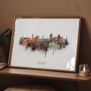Może przedstawiać: Oprawiony wydruk artystyczny przedstawiający panoramę Fort Wayne w stylu akwareli. Grafika wykorzystuje brązowe, złote i szare odcienie na białym tle. Tekst "FORT WAYNE UNITED STATES" jest wydrukowany na dole.