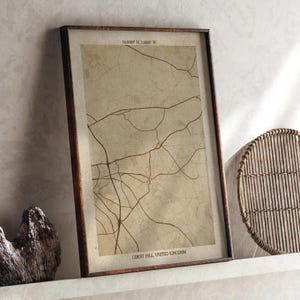 May include: A framed map print of Corby Hill, United Kingdom, in a neutral colour scheme. The map shows a network of brown lines representing roads. The print is in a dark brown frame and is displayed on a white shelf.