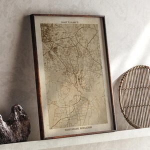 Könnte beinhalten: Gerahmter Karten-Druck von Narayanganj, Bangladesch, in Sepia-Tönen. Die Karte zeigt detaillierte Straßenlayouts und geografische Merkmale. Koordinaten sind oben angezeigt. Der Druck befindet sich in einem dunkelbraunen Rahmen.