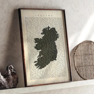 May include: Framed print of Ireland with a dark silhouette of the island. The background is filled with text, and the frame is a dark brown. The word "IRELAND" is at the top of the print.