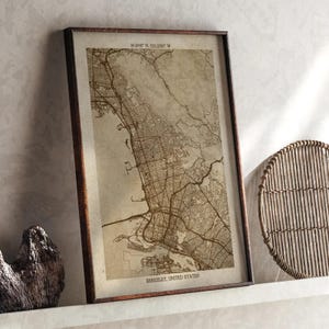 May include: A sepia-toned framed map print of Berkeley, United States. The map shows the city's layout, including roads and waterways. The dark brown frame surrounds the print, which includes the coordinates 37.8915° N, 122.2930° W.