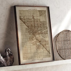 May include: A framed map of Modesto, United States, in a brown wooden frame. The map is a detailed, vintage-style depiction of the city's layout, with streets and landmarks visible. The text "37.6388° N, 120.9937° W" and "Modesto, United States" are printed on the map.