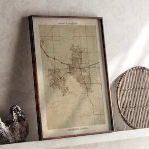 Puede incluir: Un mapa enmarcado de Lethbridge, Canadá, en un marco de madera marrón. El mapa está en tonos sepia, mostrando carreteras y el diseño de la ciudad. Las coordenadas están en la parte superior. El texto "Lethbridge, Canadá" está en la parte inferior.